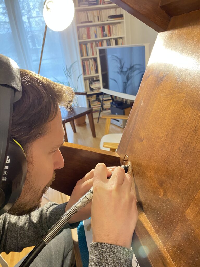 Casque sur les oreilles, Mathieu grave au dremel un numéro en dessous d’une pièce en bois massif.