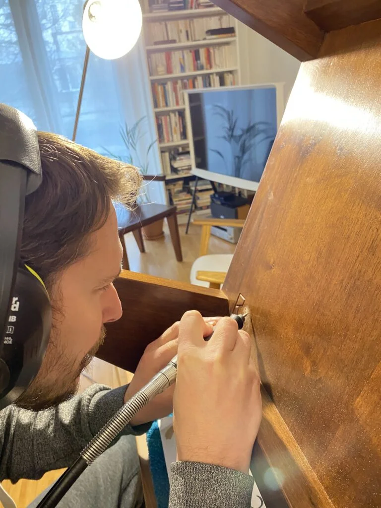 Casque sur les oreilles, Mathieu grave au dremel un numéro en dessous d’une pièce en bois massif.