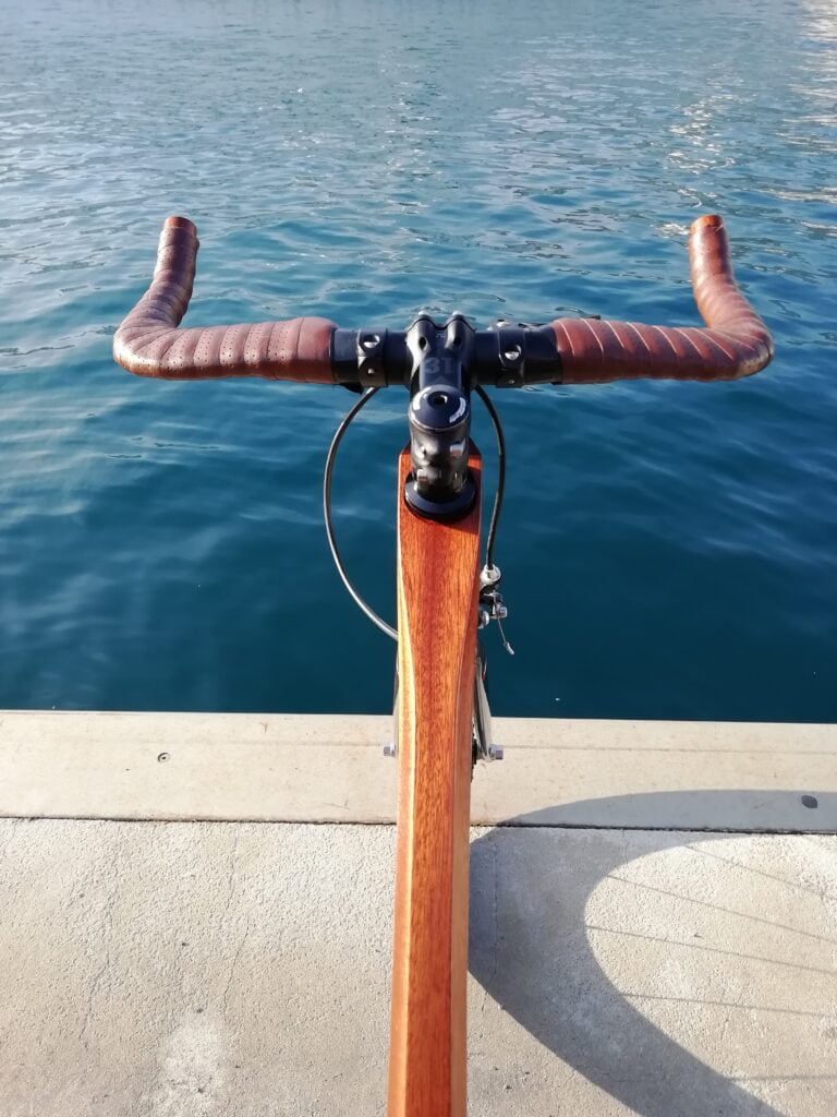 Vélo en bois vue de haut face à la mer. Ombre de la roue sur le sol.