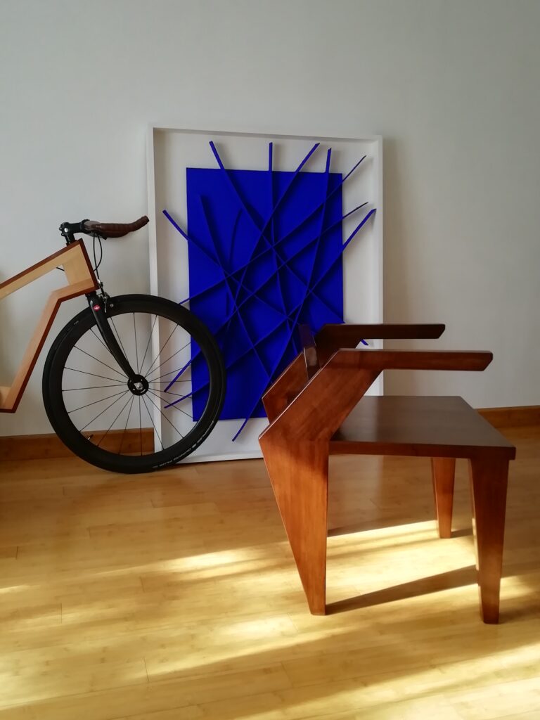 Fauteuil en bois massif a coté d’une bicyclette en bois et un tableau bleu de Galassi.